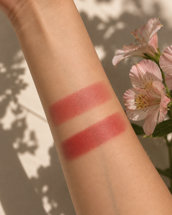 Two horizontal swatches of a rosy red cosmetic product applied on a person's forearm, with soft pink flowers and leaf shadows in the background.